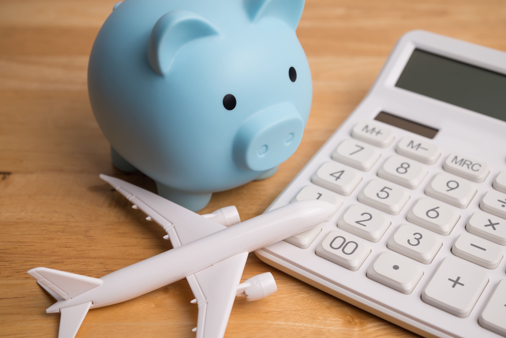 Blue piggy bank, airplane and white calculator on wooden table background.