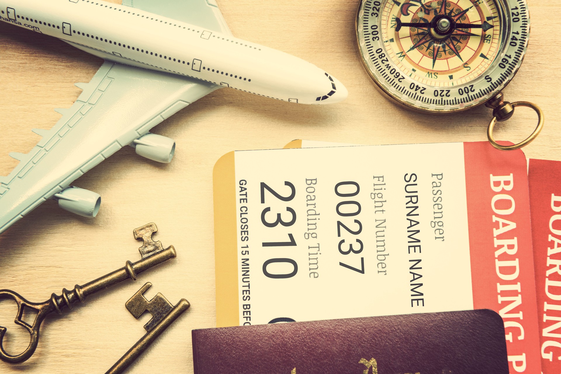 Two boarding passes with passports, vintage brass keys, a compass, a white model airplane on a table.